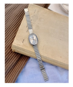 Macro view of a silver oval vintage quartz watch on corduroy and textured paper