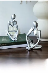 Close-up of matte silver thinker sculpture on a wooden desk with decorative books