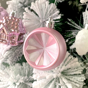 Pink round Christmas tree ornament with radial texture hanging on a snowy branch