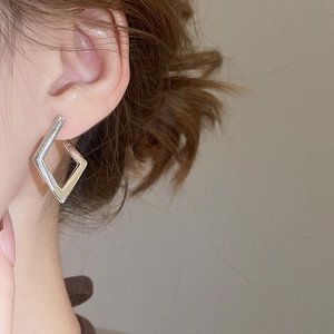 Close-up of minimalist silver geometric rhombus hoop earrings worn by a model