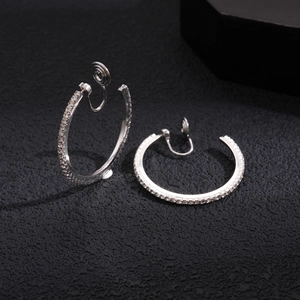 Macro shot of silver crystal-studded round ear clips on a textured black background