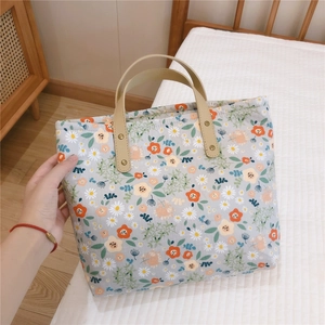 Detail of floral canvas tote bag with rivets and light beige handles on white linen