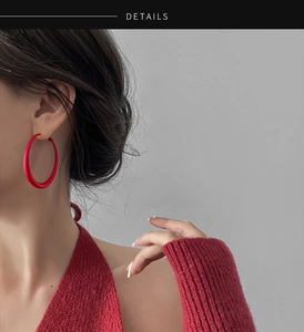 Close-up of large matte red hoop earrings worn with a matching red knit sweater