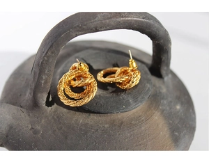 Close-up of vintage gold twist knot earrings placed on a rustic ceramic jar lid