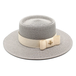Detailed view of grey boater hat featuring beige ribbon and golden bee metallic ornament