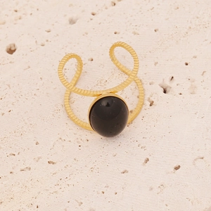 Detail of a golden double-layered hollow ring with a black oval gemstone on stone surface