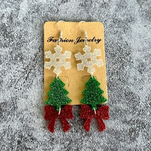 Detail of Christmas acrylic earrings with white snowflake and green glitter tree
