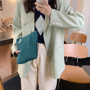 Close-up of a dark green corduroy cosmetic bag held by a model in a green suit