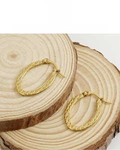 Detail of gold oval hoop earrings with honeycomb texture on wooden slices