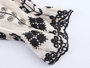 Detailed close-up of ethnic floral embroidery and scalloped cuffs on linen dress