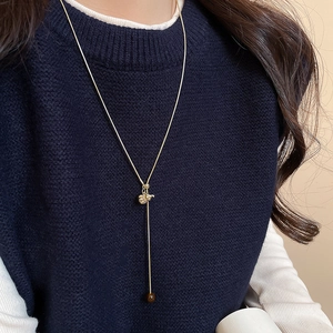 Detail view of long Y-shaped golden necklace with elephant pendant and brown bead on model