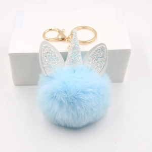 Detail of light blue fluffy unicorn pompom keychain with golden metal ring and glitter horn