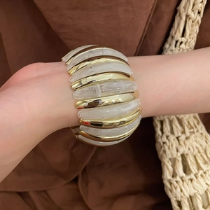 Close-up of a wide elastic bracelet featuring gold metal and marble resin blocks on wrist