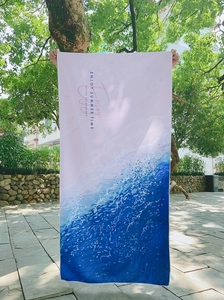 Outdoor detail showing large rectangle beach towel with blue ocean wave gradient and text
