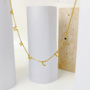 Detalle del collar dorado con letras EMANCO y una piedra preciosa azul brillante