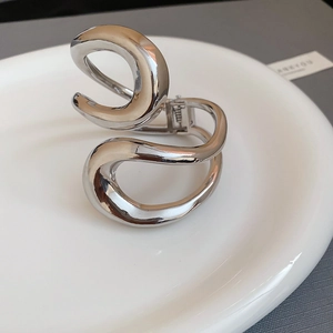 Close-up of a silver liquid metal hair claw clip with irregular wavy design on a tray