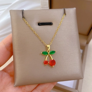 Detailed close-up of a gold necklace featuring red cherry pendants with green leaf accents