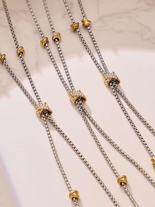 Détail de colliers ajustables en acier bicolore avec charmes sertis de zircons blancs étincelants