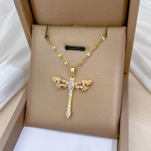 Macro shot of gold dragonfly pendant with white zircon stones on silk in a gift box