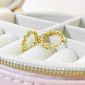 Elegant gold twisted hoop earrings with pave diamonds on a grey velvet jewelry tray
