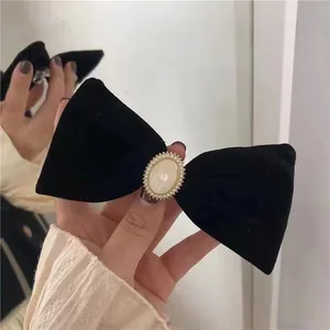 Detailed close-up of a black velvet bow hair clip featuring an elegant faux pearl centerpiece
