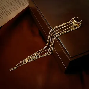 Irregular C-shaped gold tassel ear cuff with long metallic chains on a leather box