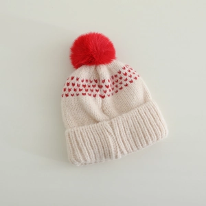 Détail du bonnet en tricot crème avec motifs de cœurs rouges et pompon en fausse fourrure
