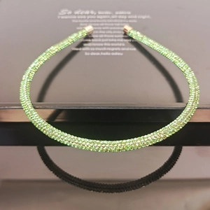 Macro shot of thin green rhinestone headband with gold tips on a glossy black surface
