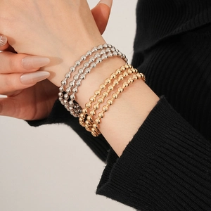 Dettaglio di modella che indossa tre braccialetti a perline oro e tre argento multistrato