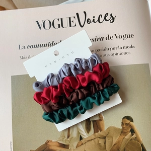 Close-up of four satin silk scrunchies in gray, red, brown, and green on a display card