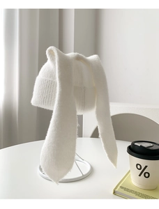 Detail of white knit bunny hat with long ears on a stand with minimalist cozy props