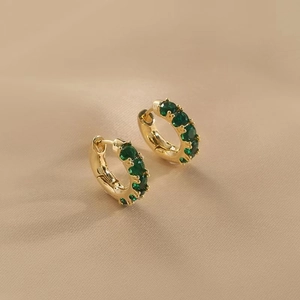 Elegant gold C-shaped hoop earrings with green zircon stones on soft fabric background