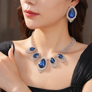 Detail of model wearing silver necklace and earrings with blue teardrop crystals