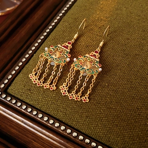 Détail de boucles d'oreilles cœur triangle en or 18 carats avec émail et pompons