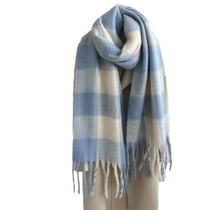 Winter mohair scarf with blue and white plaid pattern and long tassels on beige coat