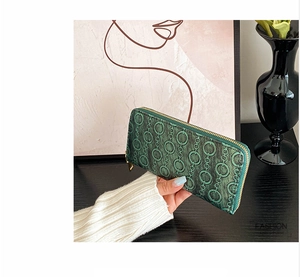 Detail of dark green long wallet featuring embossed chain patterns and gold zipper closure