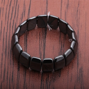 Close-up of minimalist black hematite rectangular beaded bracelet on a wooden texture