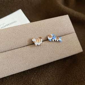 Macro shot of asymmetrical cat and fishbone stud earrings on a beige jewelry display