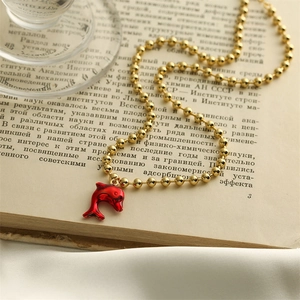 Detailed close-up of a gold bead chain with a red dolphin pendant on vintage paper