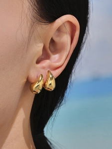 Close-up of elegant gold hollow teardrop earrings worn by a model in a summer setting