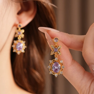 Detail shot of vintage golden earrings featuring purple oval zircon and floral design