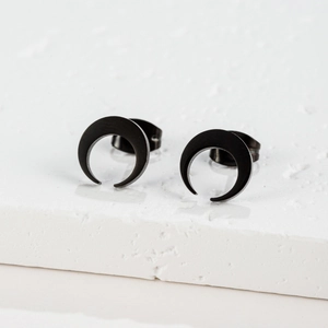 Close-up of matte black crescent moon stud earrings on a textured stone display