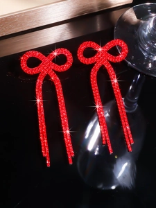 Macro detail of red bow tassel earrings featuring sparkling crystals and long pendants