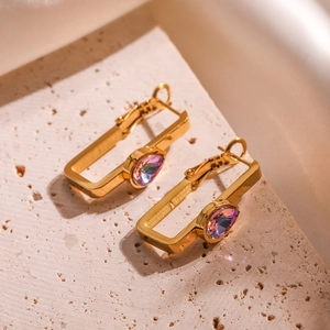 Gold rectangular earrings with pear-cut purple zircon on a textured stone surface