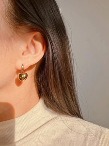 Close-up of model wearing gold heart earrings with red enamel and vintage charm