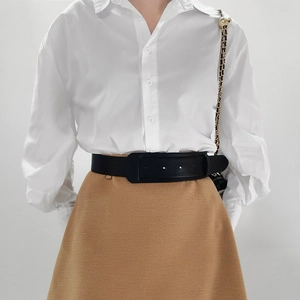 Detail of a minimalist black wide leather belt with gold buckle and adjustable holes