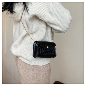 Detail shot of a black croc-effect small crossbody bag with gold chain and metal buckle
