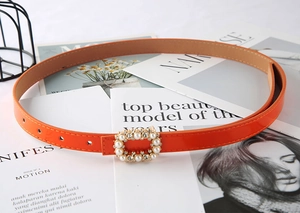 Detailed macro view of orange PU leather belt with pearl and rhinestone buckle decoration