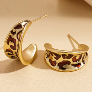 Macro view of C-shaped gold metal earrings with leopard print enamel texture