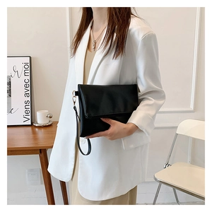 Detalle de bolso de mano tipo sobre negro con correa junto a un traje blanco de mujer